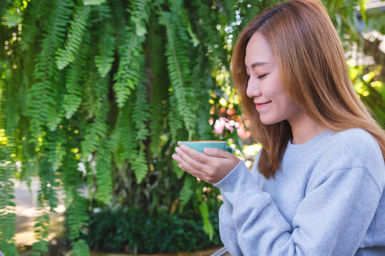 Portrait image of a beautiful young asian woman holding and drinking hot coffee in the outdoors