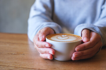 Closeup image of a woman holding coffee cup on wooden table