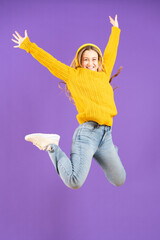 Full length studio shot of happy pretty young woman jumping on air isolated on purple background