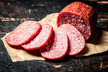 Sliced salami sausage on paper on the table.