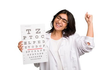 Young indian oculist woman holding an eye chart paper cut out isolated raising fist after a...
