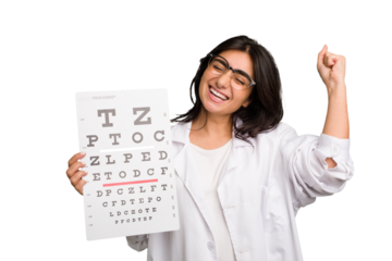 Young indian oculist woman holding an eye chart paper cut out isolated raising fist after a victory, winner concept.