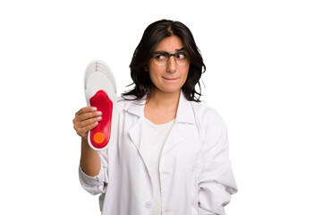 Young indian chiropodist woman holding a insoles for shoes cut out isolated confused, feels doubtful and unsure.