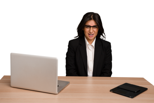 Young indian woman in a table with a laptop and tablet isolated shouting very angry, rage concept, frustrated.