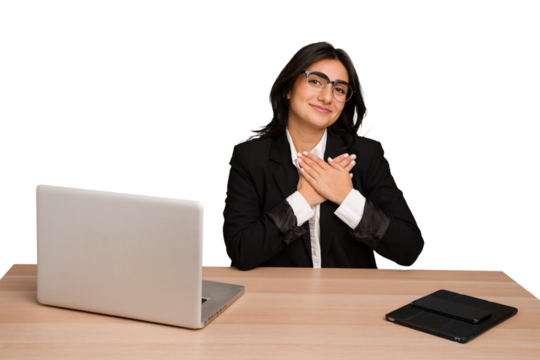 Young indian woman in a table with a laptop and tablet isolated has friendly expression, pressing palm to chest. Love concept.
