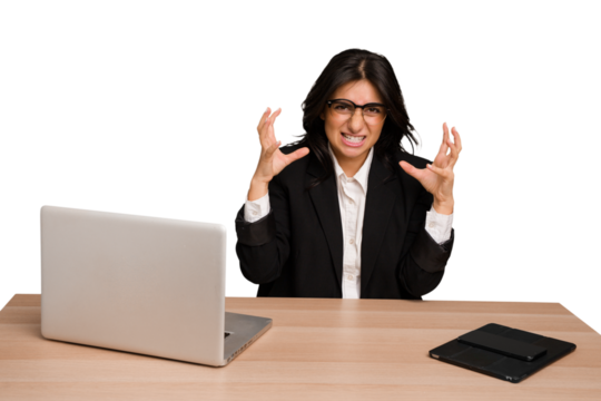 Young indian woman in a table with a laptop and tablet isolated screaming with rage.