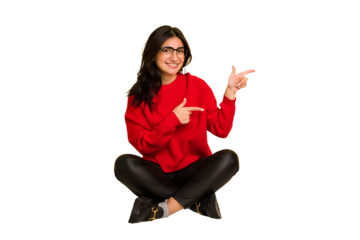 Young indian woman sitting on the floor cut out isolated excited pointing with forefingers away.
