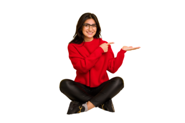 Young indian woman sitting on the floor cut out isolated excited holding a copy space on palm.