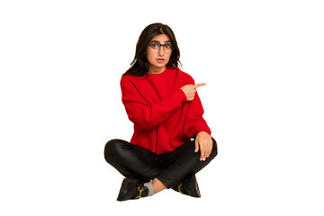 Young indian woman sitting on the floor cut out isolated pointing to the side