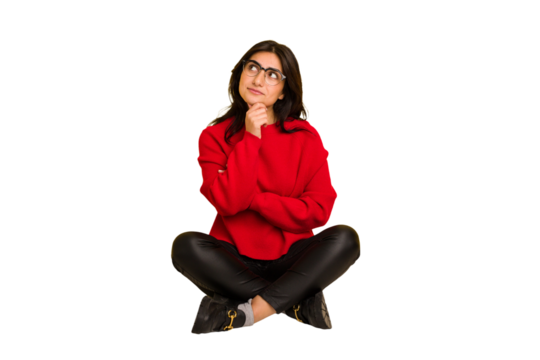 Young indian woman sitting on the floor cut out isolated looking sideways with doubtful and skeptical expression.