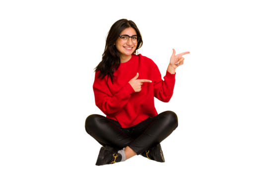 Young indian woman sitting on the floor cut out isolated excited pointing with forefingers away.