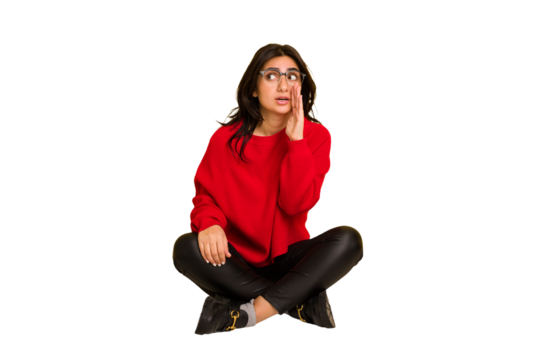 Young indian woman sitting on the floor cut out isolated is saying a secret hot braking news and looking aside