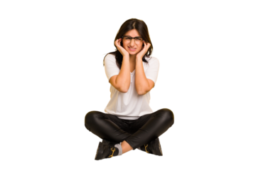 Young indian woman sitting on the floor cut out isolated covering ears with hands.