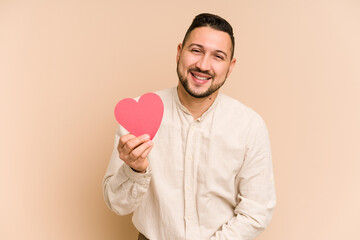 Adult latin man holding a red heart isolated laughing and having fun.