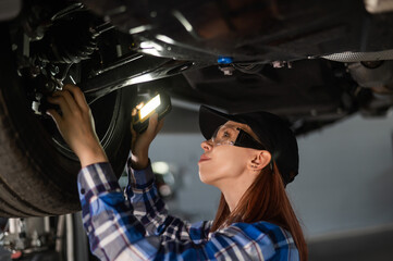 A female mechanic inspects a lifted car. A girl at a man's work.