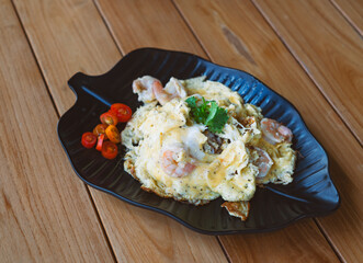 Thai food style of Scrambled eggs with shrimp over rice on a beautiful black leaf plate, decoration of small Coriander leave. Wooden table food.