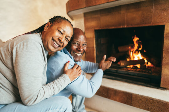 Senior african american couple warming up next to fireplace inside mountain chalet - Winter lifstyle and love concept - Main focus on woman face