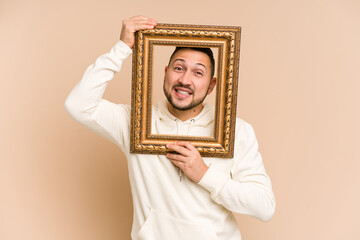 Adult latin man holding a vintage frame and smiling isolated