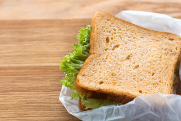 Fresh sandwich with lettuce and tomato.
Lies on a wooden plate.