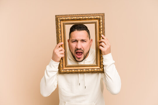 Adult latin man holding a vintage frame and smiling isolated