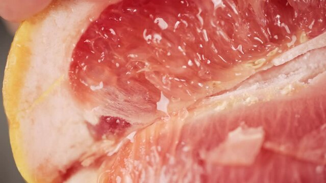 Slow motion footage of person squeezing a grapefruit. Close up view of juicy red orange fruit. Making citrus juice with hands