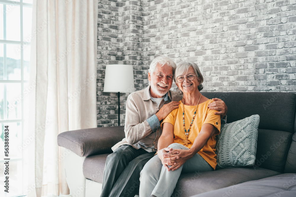 Sticker Beautiful hoary good-looking mature spouses relaxing together on comfy couch at modern home smiling staring at camera feel carefree. Good harmonic relationships, happy marriage, endless love concept.