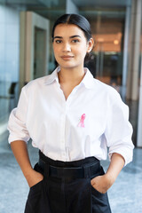 Happy South Asian put on pink ribbon on her shirt, concept of breast cancer awareness day or month