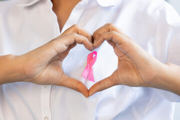 Happy South Asian woman posing heart hand gesture with pink ribbon, concept of love and care in...
