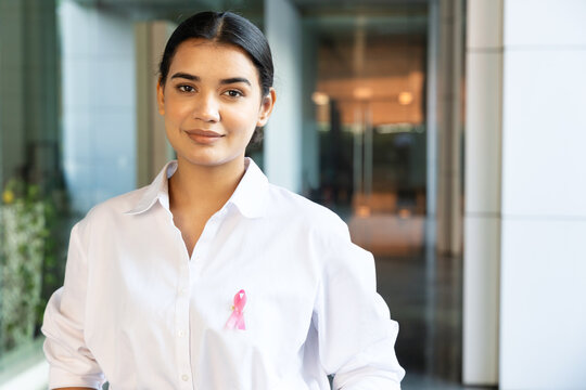 Happy South Asian put on pink ribbon on her shirt, concept of breast cancer awareness day or month