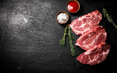 Raw pork steak on a stone board with tomato sauce, rosemary and spices. 