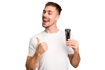 Young man holding a shaving machine cut out isolated points with thumb finger away, laughing and carefree.