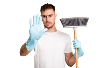 Young man holding a broom to clean his house cut out isolated standing with outstretched hand showing stop sign, preventing you.