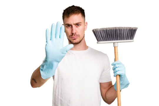 Young man holding a broom to clean his house cut out isolated standing with outstretched hand showing stop sign, preventing you.