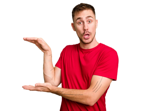 Young caucasian man cut out isolated shocked and amazed holding a copy space between hands. - Powered by Adobe