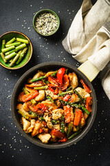 Chicken stir fry with vegetables and sesame in the skillet at black stone background. Top view,...