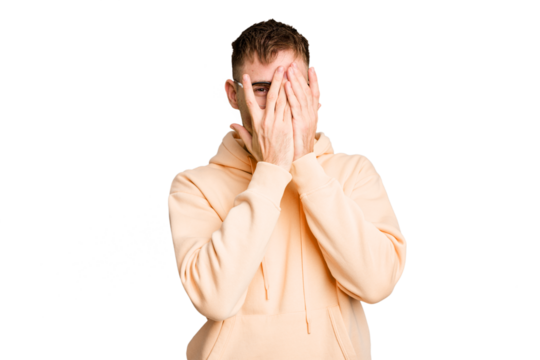 Young caucasian man cut out isolated blink through fingers frightened and nervous.