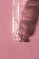 Dropper pipette with trasparent liquid on pink background with shadow.Flat lay