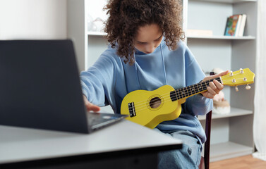 Teen girl engaged in her hobby at home, learn to play on ukulele or guitar remotely using video from Internet. She plays music, takes new skills, recreation