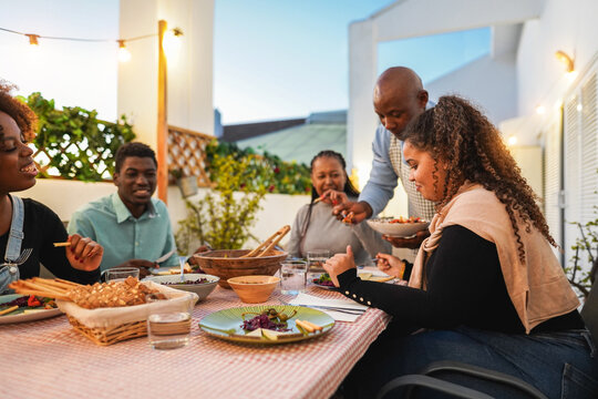 Happy african family doing dinner while eating healthy food at home patio - Lifestyle home moments and summer concept - Main focus on right girl hand