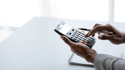 Businessman is using a calculator to calculate company financial figures from earnings papers, a...