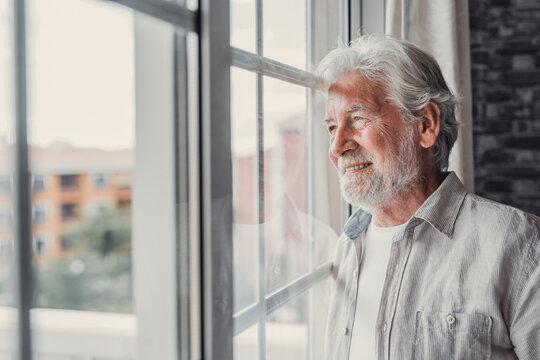 Happy thoughtful older 70s man looking out of window away with hope, thinking of good health, retirement, insurance benefits, dreaming of future. Elderly pensioner waiting meeting with family.