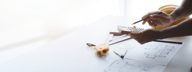 The architect is pointing to the house plans he has designed, he is meeting with engineers and...