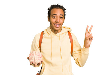 Young African American man holding a brain isolated joyful and carefree showing a peace symbol with fingers.