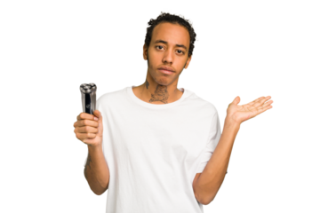 Young African American man holding a razor isolated showing a copy space on a palm and holding another hand on waist.