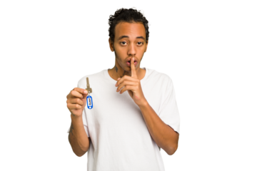Young African American man holding home keys isolated keeping a secret or asking for silence.