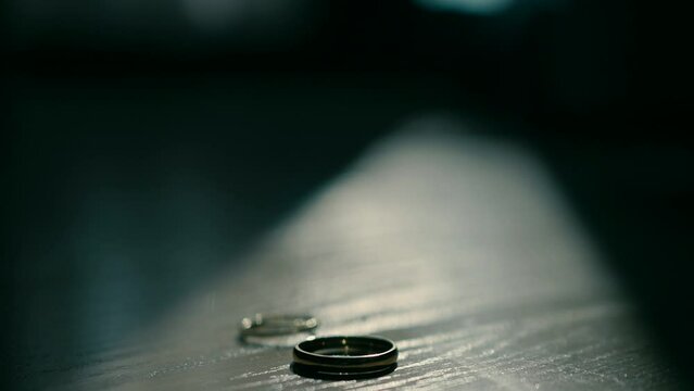Close-up of wedding rings. A man spins one ring inside another ring in the dark on the wooden table.