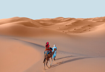 A woman in a red turban riding a camel across the thin sand dunes of the in Western Sahara Desert,...