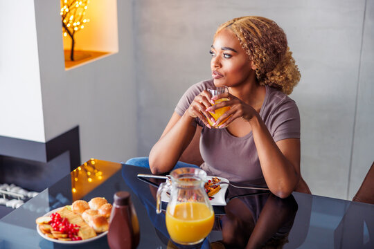 Woman drinking orange juice while having breakfast at home