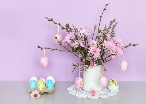 Easter still life with spring bouquet of pussy-willow twigs and pink fresh chrysanthemum flowers and traditional painted Easter eggs on pastel pink  background. Greeting card, festive message