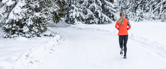 Running in winter, rear view of a female runner on a snowy path in a park or forest